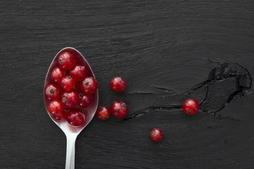 Spoonful of red currants on black wooden background