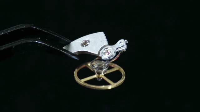 Watch movement or mechanism component , the balance wheel with the metallic hairspring attached to bridge piece , isolated on black background