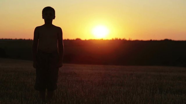 The boy at sunset does exercises running around the field. The child at the sunset of the day in the field runs and does exercises.
