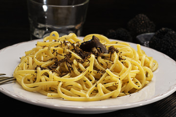 Strangozzi, italian wheat pasta with black truffle on a black wooden board.