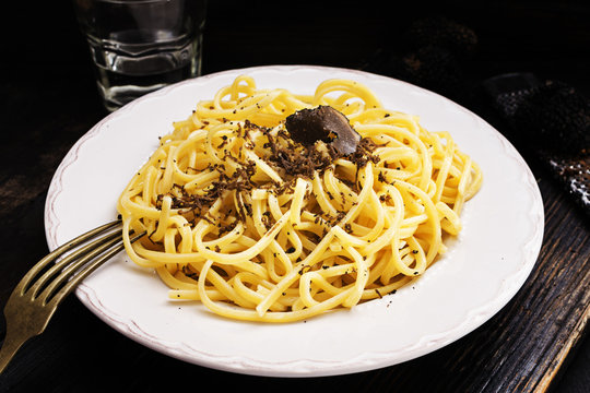 Strangozzi, italian wheat pasta with black truffle on a black wooden board.