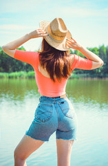 Fototapeta na wymiar Sexy hot young woman with full hips thin waist pale skin, in cut shorts red top and straw hat posing on nature outdoor at warm summer day