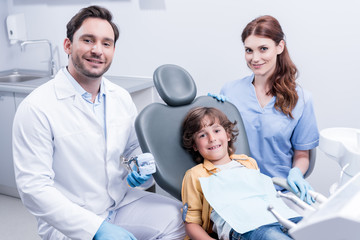 Obraz premium little boy sitting in chair with smiling dentists in dental clinic