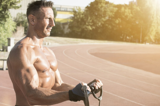 Handsome middle aged man working out on a running track. Healthy adult man doing biceps workout. Tanned skin and shirtless middle-aged man.