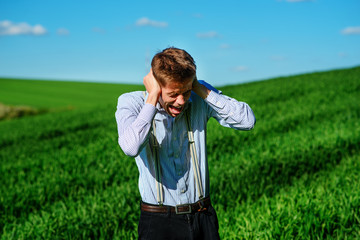 Handsome man in the field is closing his ears with his hands:trying to ignore, not to hear something