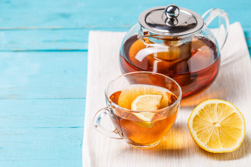 Glass cup of tea with lemon and glass teapot.