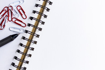 pen, paper clip and white notebook on wooden table.