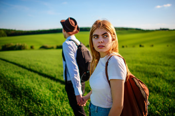 A pair of lovers are holdings their hands together on a green field. Attractive man and a beautiful woman are walking between meadow