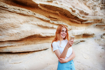 Beautiful woman smiling and looking at the screen of a smartphone on the background of a sand quarry