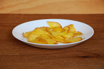 Dried and fried cassava slices place on white plate isolated on wood texture background. This is local Malaysian traditional junk food call Kerepek Ubi.  
