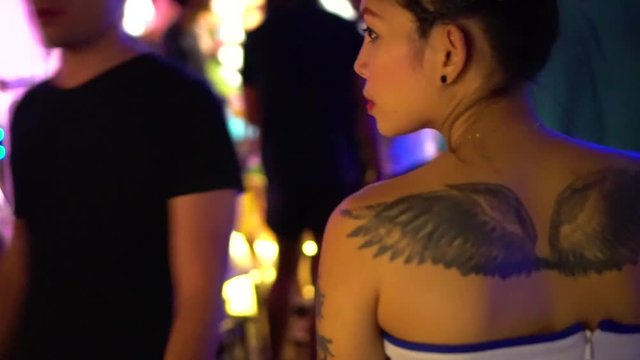 Beautiful thai girl with a tattoo on her back, looks around in a nightclub.
