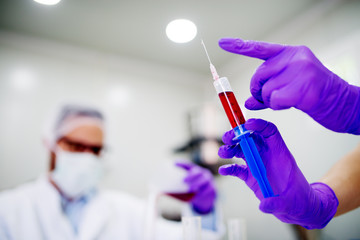 Close up of a doctors hand holding syringe with blood. Analyzing blood in the laboratory.