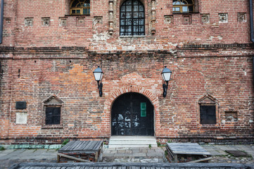 Forged lantern on a brick wall. Old red brick building with black metal door and windows © Mak