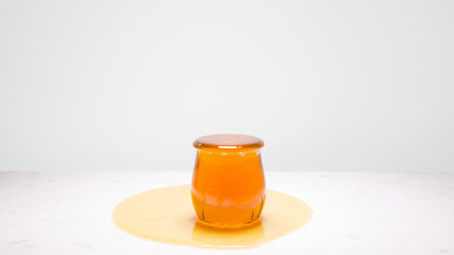 My cup runneth over - a jar overflowing with honey on a white marble countertop and copy space above, to the left and right.