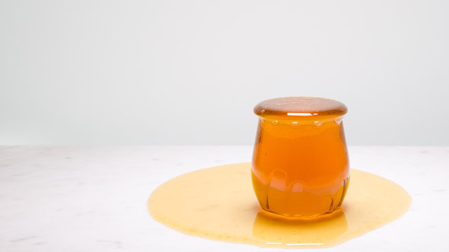 My cup runneth over - a jar overflowing with honey on a white marble countertop and copy space to the right.