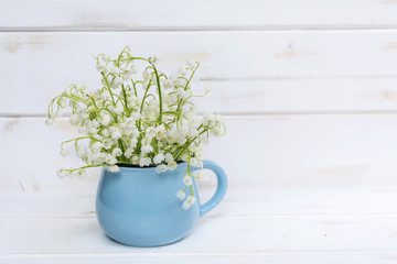 Lily of the valley bouquet in vase on a white wooden background