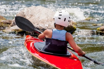 A teenager trains in the art of kayaking. Boat boats on rough river rapids. The child is skillfully engaged in rafting.