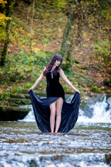 Cute brunette standing in a river and holding a black dress