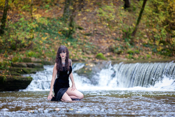 Fototapeta premium Cute brunette standing in a river and holding a black dress