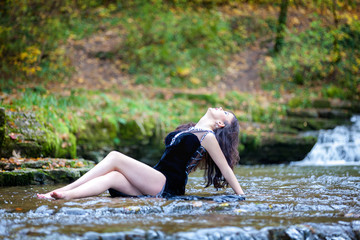 Cute brunette sitting in river raising legs and holding black dress
