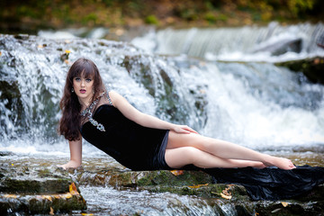 Cute brunette sitting in river raising legs and holding black dress