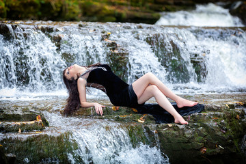 Cute brunette sitting in river raising legs and holding black dress