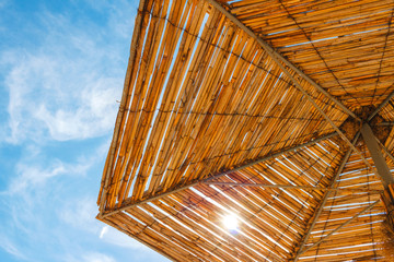 View under straw beach umbrella on blue and cloud sky background