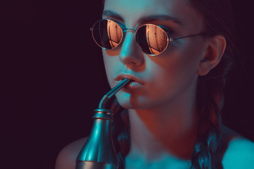 woman in round sunglasses drinking soda from water bottle with straw