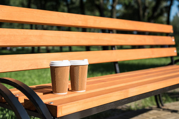 Close-up view of two disposable coffee cups on wooden bench in park