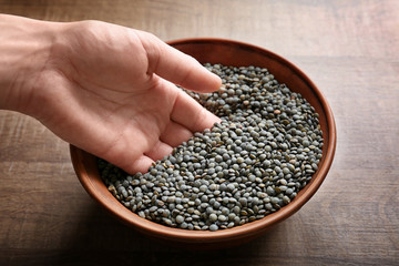 Female hand with black lentils in bowl on wooden background