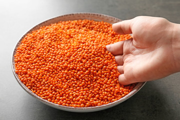 Female hand with red lentils in bowl on grey background