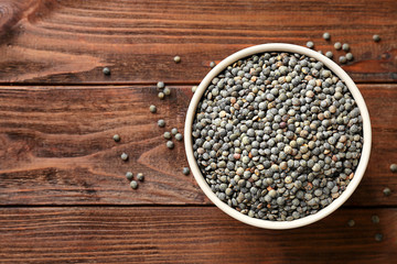 Bowl with black lentils on wooden background