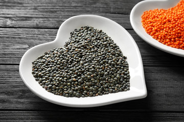 Plates with black and red lentils on wooden background
