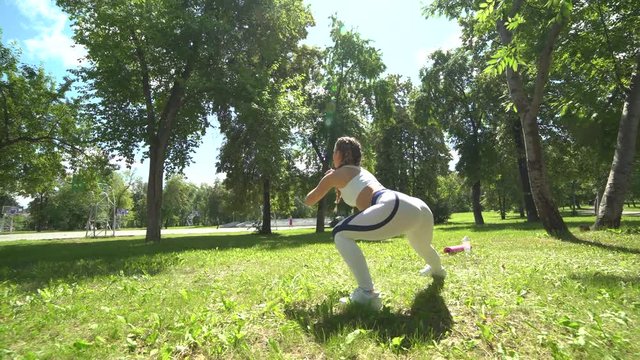 Young female athlete doing squat exercises outdoors in park. Fit girl working out her core and glutes with bodyweight.