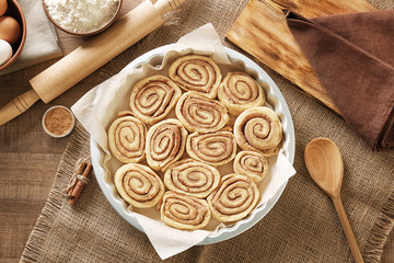 Raw cinnamon rolls in baking pan and ingredients on kitchen table