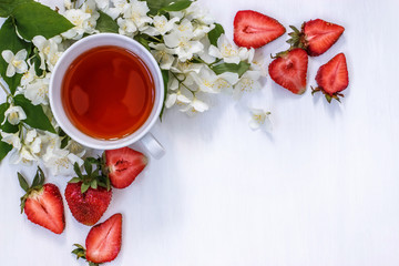 Cup of black tea with aromatic Jasmine flowers and strawberries on white background