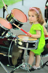Fototapeta na wymiar One year old cute girl in a green embroidered romper learning to drum outdoors