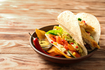 Tasty fish taco on plate with sauce and chips on wooden background