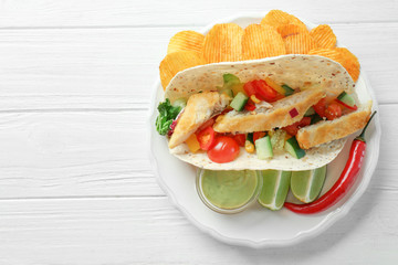 Tasty fish taco on plate with sauce and chips on white wooden background
