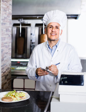 mature man cook taking order from customer on counter in fast food restaurant