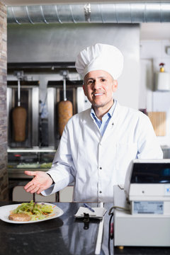 Chef wearing uniform holding plate with made kebab