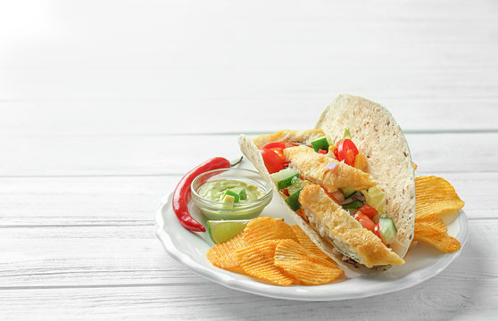 Tasty fish taco on plate with sauce and chips on white wooden background