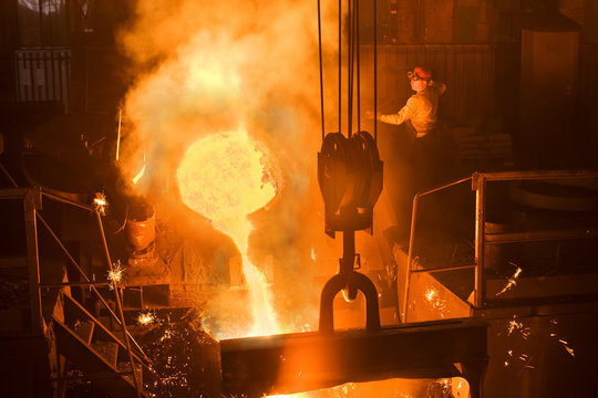 Working in a foundry. Worker looking down, red color is a reflection of the molten metal. Very high heat and purple fringing. See more images and video from this series.