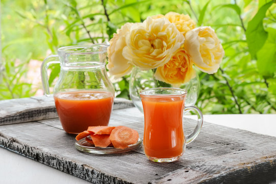 Carrot juice in pitcher and glass transparent glass on a background of roses.