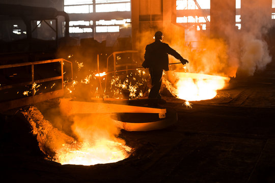 Working in a foundry. Worker looking down, red color is a reflection of the molten metal. Very high heat and purple fringing. See more images and video from this series.