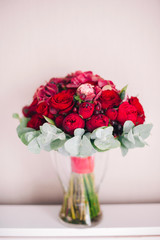 wedding bouquet of red flowers and David Austin roses is in a vase on a white table