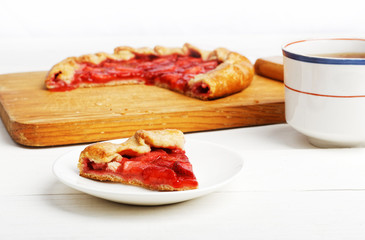 Piece of homemade pie with strawberries and cup of tea on white wooden table. Shallow focus.