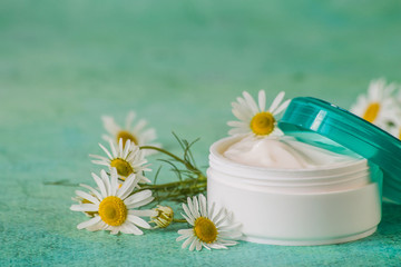 Obraz na płótnie Canvas Natural cosmetics. A jar with cream for face and body skin care and fresh chamomile flowers on a green background.