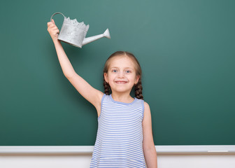 Schoolgirl with watering can play near a blackboard, empty space, education concept © soleg