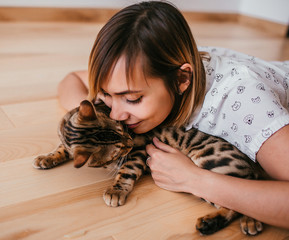 Woman plays with Bengal cat on the floor in the kitchen